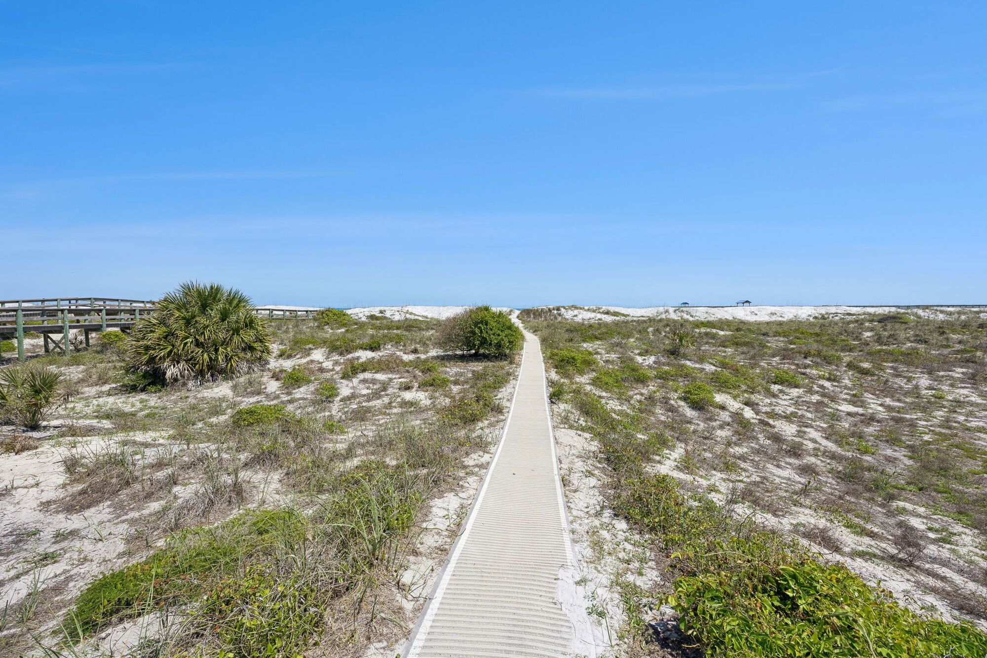 Un sentier sablonneux menant à une plage, avec une promenade en bois et un pont également en bois.
