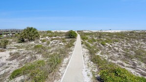 En sti af sand der fører til en strand med en træpromenade og en træbro.
