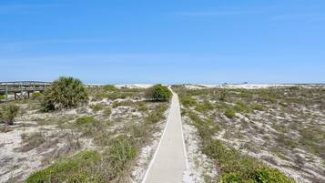Un sentier sablonneux menant à une plage, avec une promenade en bois et un pont également en bois.
