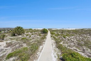 A sandy path leading to a beach with a wooden boardwalk and a wooden bridge.