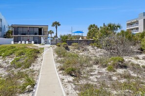 A pathway leading to a building with a beach view, a blue umbrella, and a sign indicating a beachside location. - Beachside Motel Ocean Front Kitchen Suite (Fernandina Beach)