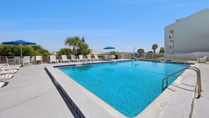 A swimming pool with lounge chairs and umbrellas, surrounded by a fence and palm trees.