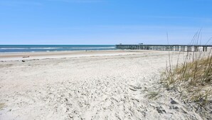 A beach with a pier extending into the water, sandy beach, and clear skies.