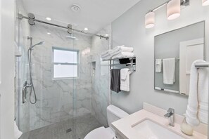 A modern bathroom with a glass-enclosed shower, a white toilet, and a sink with a mirror.