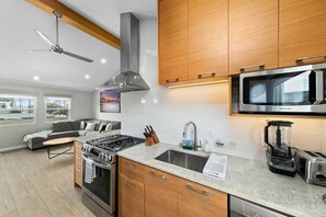 A modern kitchen with a gas stove, oven, microwave, and a built-in dishwasher. There is a wooden cabinet above the sink and a ceiling fan. - Modern, Newly Renovated 2BR Apt in Heart of OB (San Diego)