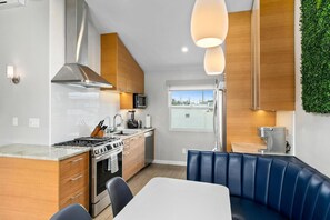 A modern kitchen with wooden cabinets, a gas stove, and a built-in microwave. There is a dining area with a blue booth and a white table.