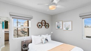 Une chambre à coucher comprenant un lit, une table de chevet, un ventilateur de plafond et une fenêtre donnant sur l’extérieur.