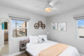 A bedroom with a bed, a nightstand, a ceiling fan, and a window with a view of the outside.