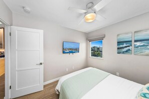A bedroom with a bed, a ceiling fan, a window with a view, and a door.