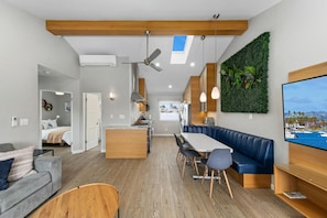 A modern kitchen with a central island, a dining area with a blue booth, and a living space with a grey sofa and wooden coffee table. - Modern, Newly Renovated 2BR Apt in Heart of OB (San Diego)