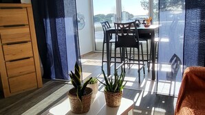 Un soggiorno con un tavolino bianco, due piante in vaso, un mobile in legno e vista su un'area pranzo esterna attraverso una porta vetrata.
