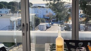 Un tavolo con una bottiglia, un bicchiere da vino e tazze da caffè, con vista su edifici e alberi.
