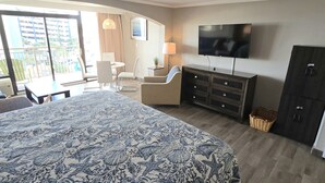 A hotel room with a large bed, a TV, a desk, and a balcony with a view of buildings. - Caravelle 505 Ocean view Efficiency w/pools (Myrtle Beach)