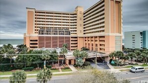 A multi-story hotel with a central atrium, a parking garage, and a view of the ocean. - Caravelle 505 Ocean view Efficiency w/pools (Myrtle Beach)