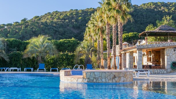 Un espace piscine comprenant des chaises longues, une piscine en pierre et un bâtiment doté d’une terrasse.