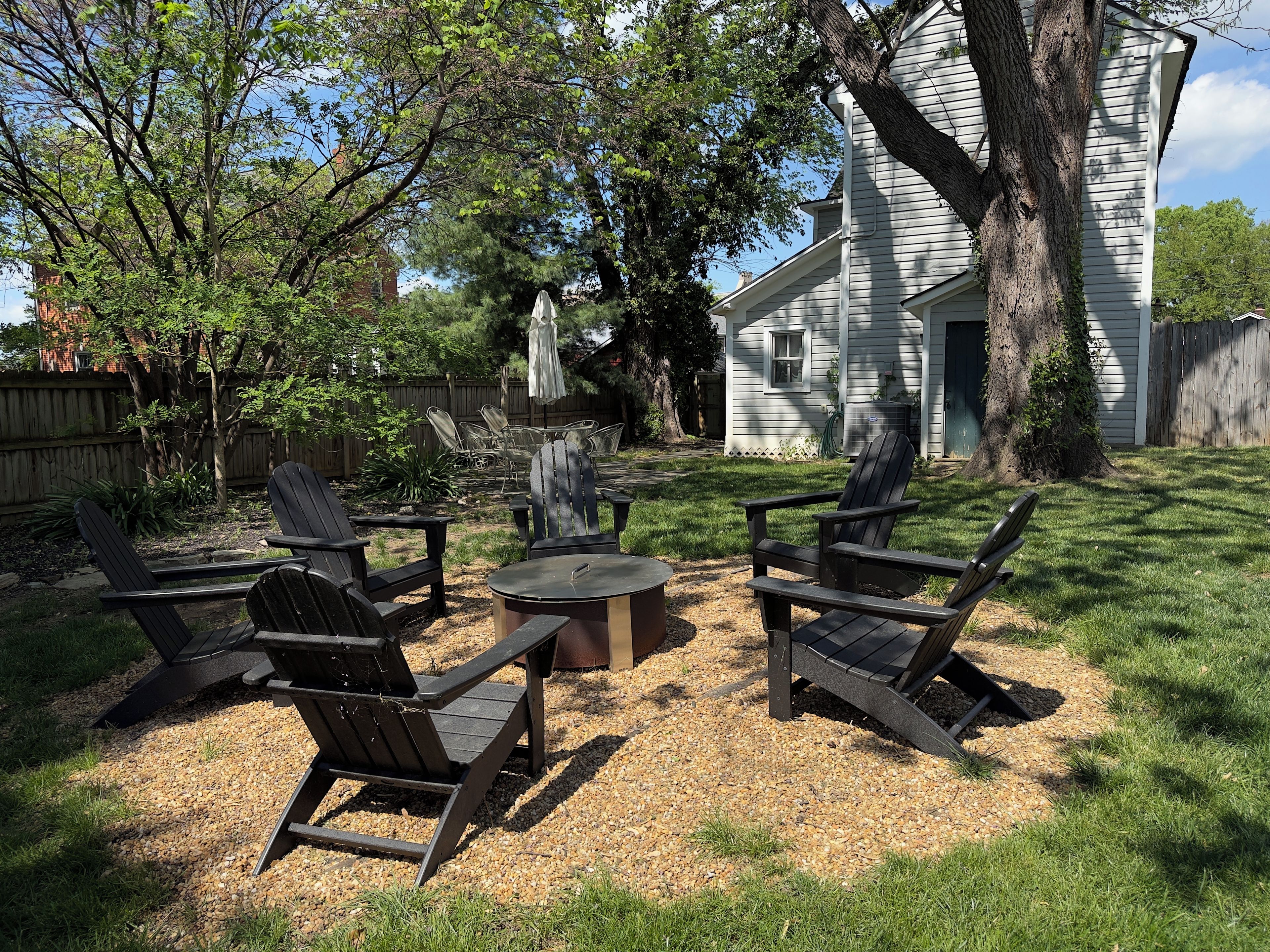 A backyard with a fire pit, four Adirondack chairs, and a wooden table.