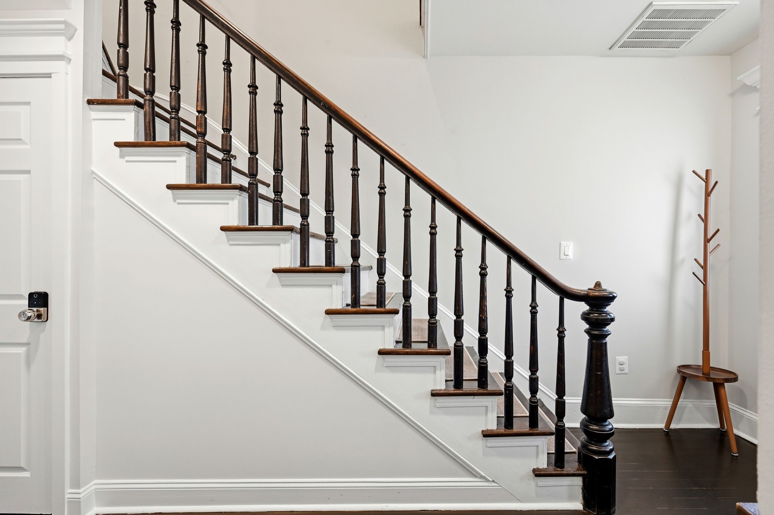 A staircase with wooden balusters and a handrail, leading to a landing with a coat rack.