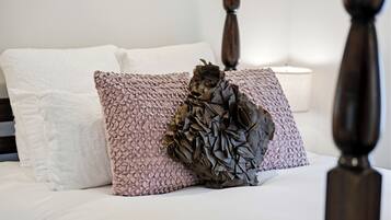 A bed with a white and pink textured pillow, a decorative leaf-shaped pillow, and a white bedside lamp.