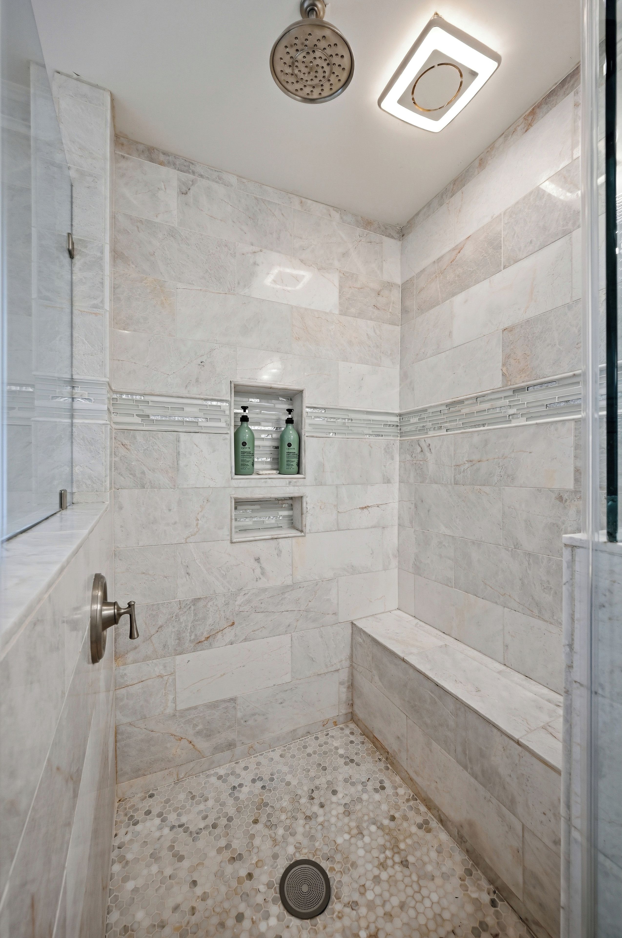 A walk-in shower with marble walls, a built-in bench, and a showerhead.