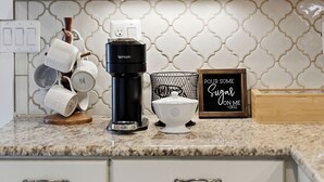 Een keuken met witte kasten, een koffiezetapparaat, mokken en een bordje met de tekst 'Pour some sugar on me'.