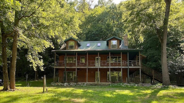 A two-story log cabin with a balcony, surrounded by lush greenery.