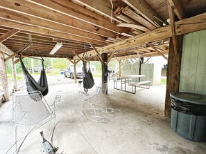 Ett takförsett utomhusområde med ett picknickbord, metallstolar, en hängmatta och en soptunna.