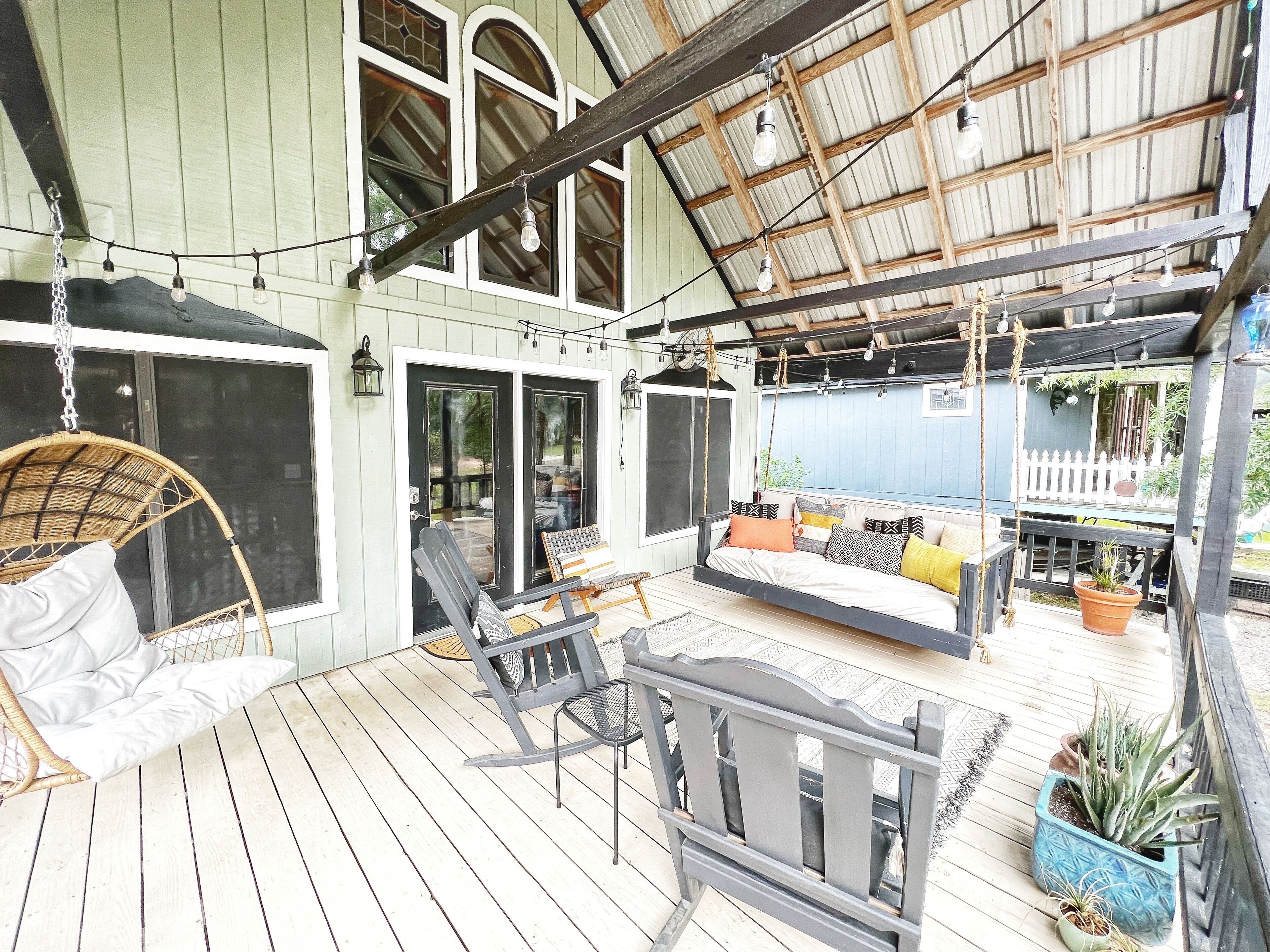 A covered outdoor seating area with a swing chair, a sofa with cushions, and potted plants.