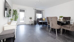 A modern living room with a sofa, a dining table with chairs, a bench, and a small side table with a plant. - Stylish House with Garden & Parking (Glasgow)