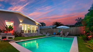 A backyard with a swimming pool, a covered patio, and a wooden fence. - Family Beach Retreat | Pool + Golf Cart (Jacksonville Beach)