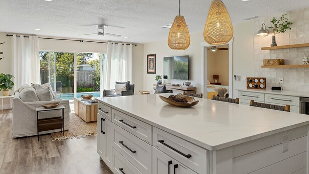 A modern kitchen with a large island, pendant lights, and a view to the outdoor area. - Family Beach Retreat | Pool + Golf Cart (Jacksonville Beach)