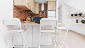 A modern kitchen with a central island, white bar stools, and a brick accent wall.