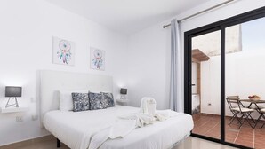 A hotel room with a large bed, two wall-mounted lamps, and a view of the outdoor patio.