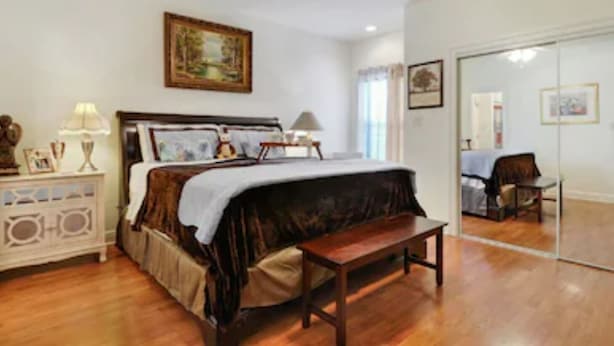 A bedroom with a bed, bedside tables, a lamp, a painting on the wall, and a mirror.