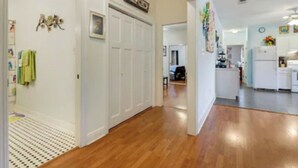 A hallway with wooden flooring, white doors, and a kitchen area with white appliances.