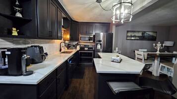 A modern kitchen with dark cabinetry, a white countertop, a built-in oven, a microwave, and a refrigerator.