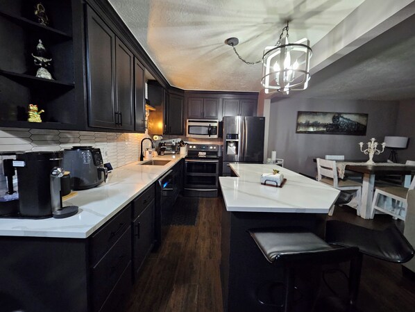 A modern kitchen with dark cabinetry, a white countertop, a built-in oven, a microwave, and a refrigerator.