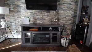 Een moderne woonkamer met een wand met stenenreliëf, een wandgemonteerde flatscreen-tv, een donkere houten entertainmentkast en een klein beeldje.