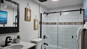 Un baño moderno con cabina de ducha de vidrio, un lavabo blanco y un inodoro.