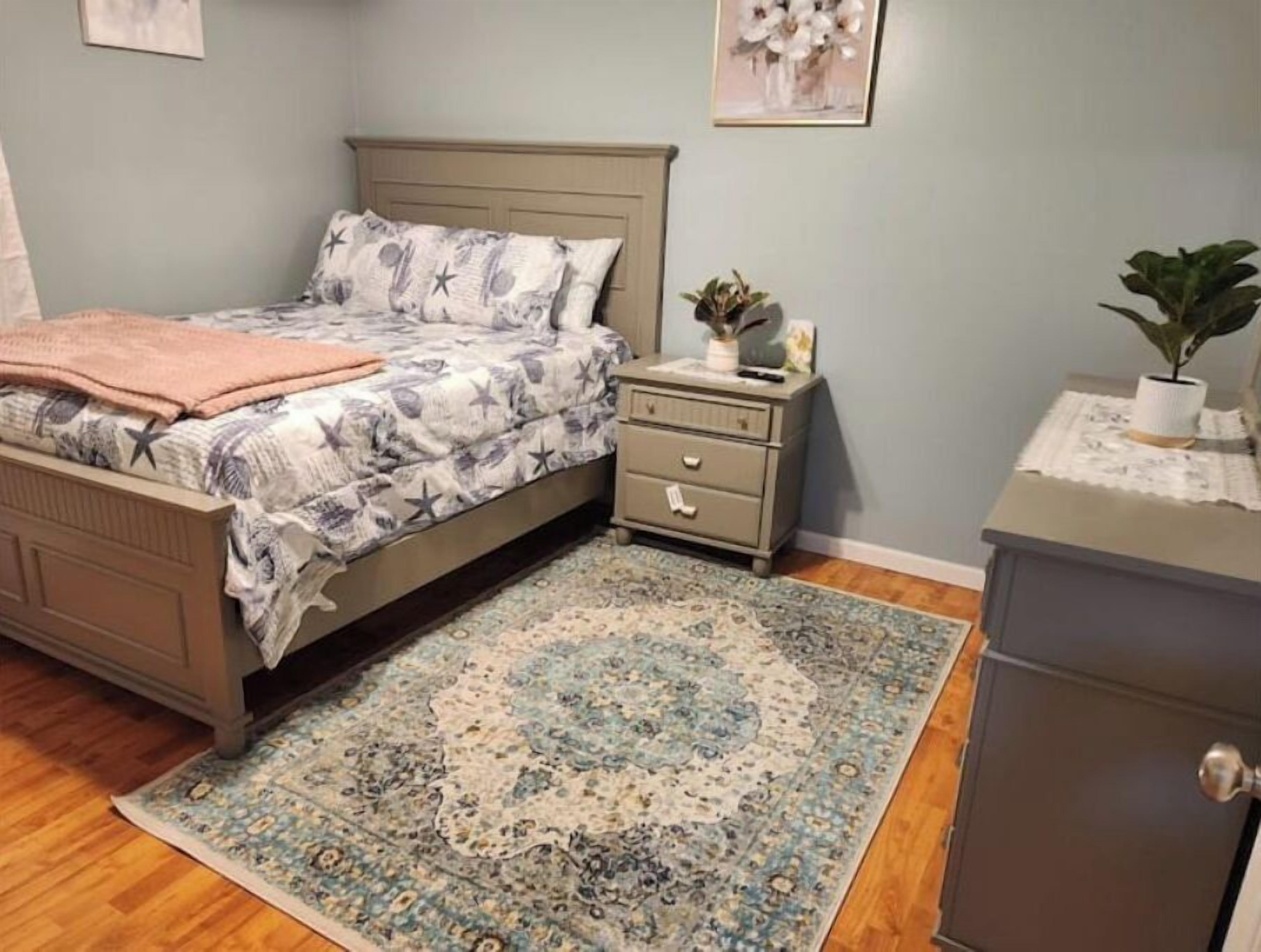 A bedroom with a bed, nightstand, dresser, and a patterned rug.