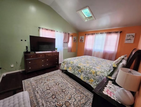 Ein Schlafzimmer mit Bett, Kommode, Fernseher und Deckenleuchte.
