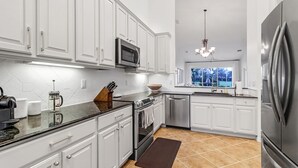 A modern kitchen with white cabinetry, stainless steel appliances, and a large window offering a view of the outdoors. - The House on Castlelawn (Naples)