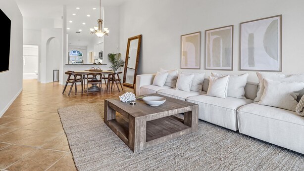A spacious living room with a white sofa, a wooden coffee table, and a dining area with a chandelier. - The House on Castlelawn (Naples)