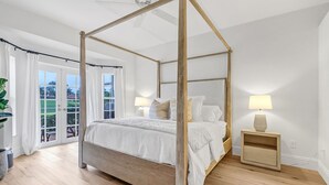 A bedroom with a four-poster bed, a nightstand with a lamp, and a view of the outdoors through a glass door. - The House on Castlelawn (Naples)