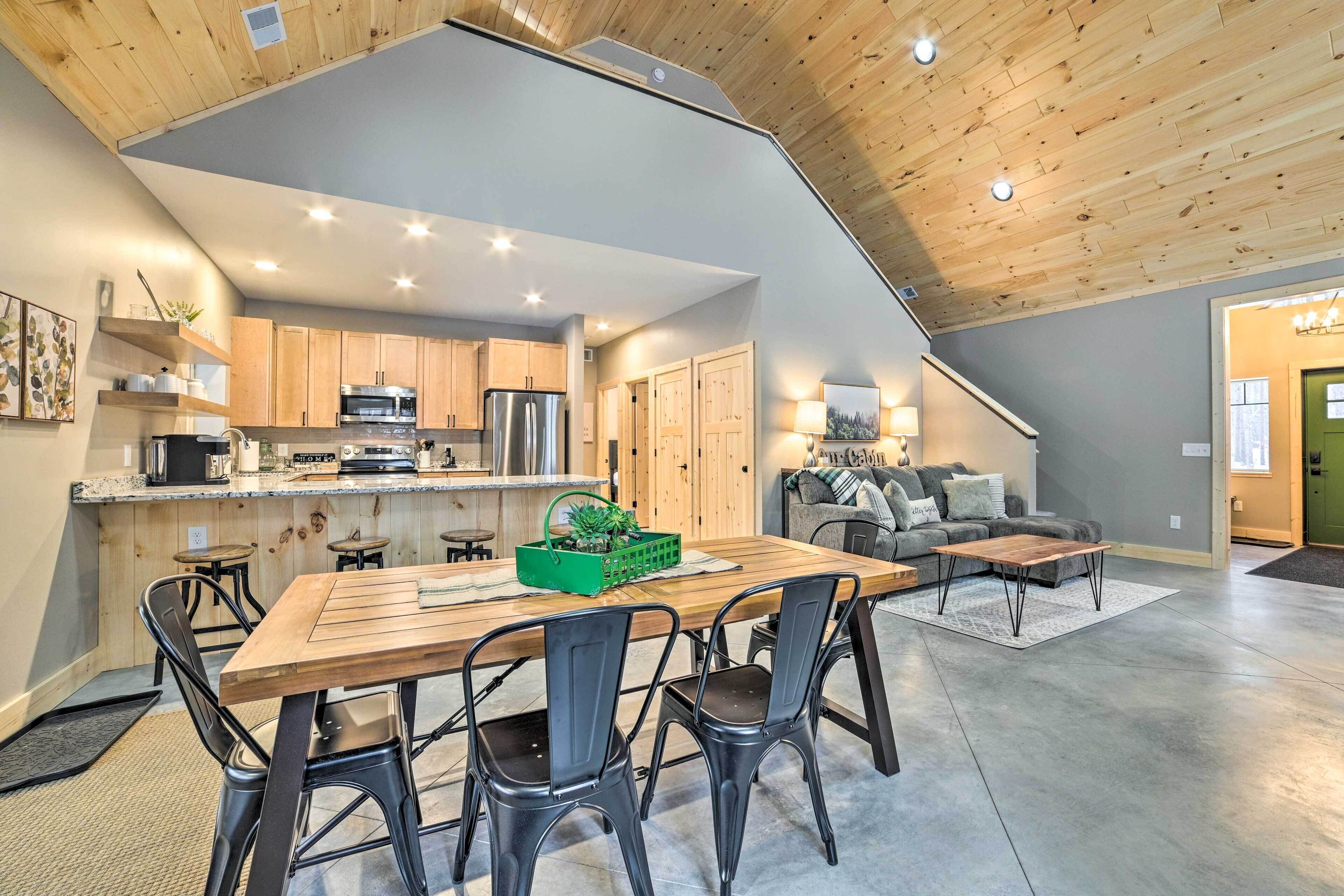 A spacious living area with a wooden dining table, black chairs, a sofa, and a kitchen with wooden cabinets and modern appliances.