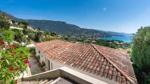 Un edificio de estilo mediterráneo con techos de tejas de terracota, rodeado de exuberante vegetación y con vistas a un pueblo costero.