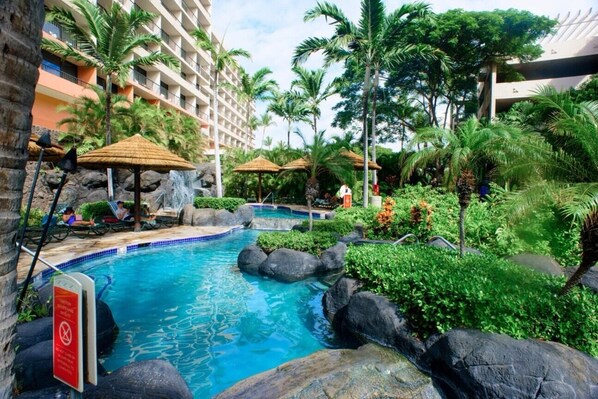 Un espace piscine aménagé avec des chaises longues, des parasols et des plantes tropicales.