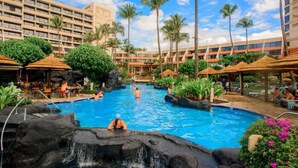 A resort pool with a waterfall feature, surrounded by palm trees and outdoor seating areas. - Maui Resort Rentals: Marriott's Maui Ocean Club Studio Oceanfront Suite (Lahaina)