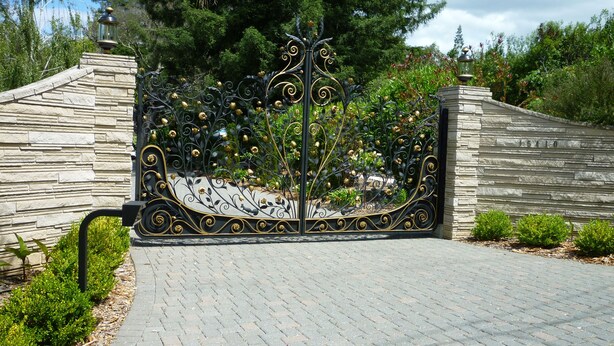 A wrought iron gate with intricate designs, leading to a stone wall with a number plaque.