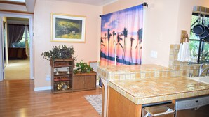 A kitchen with a tiled countertop, a dishwasher, and a window with a curtain.