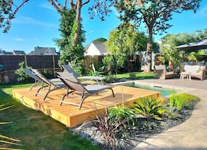 A backyard with a wooden deck, lounge chairs, a small pool, and surrounding greenery.